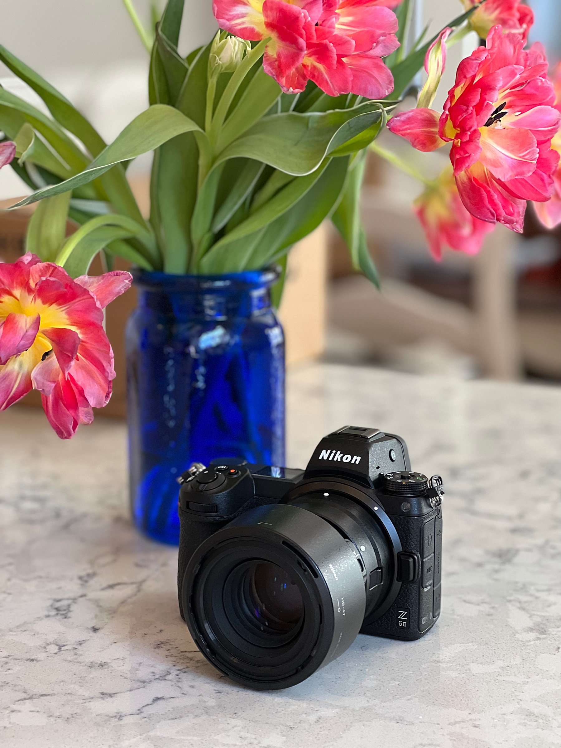 Nikon mirrorless camera with attached lens resting on a marble surface beside a cobalt blue vase of tulips.
