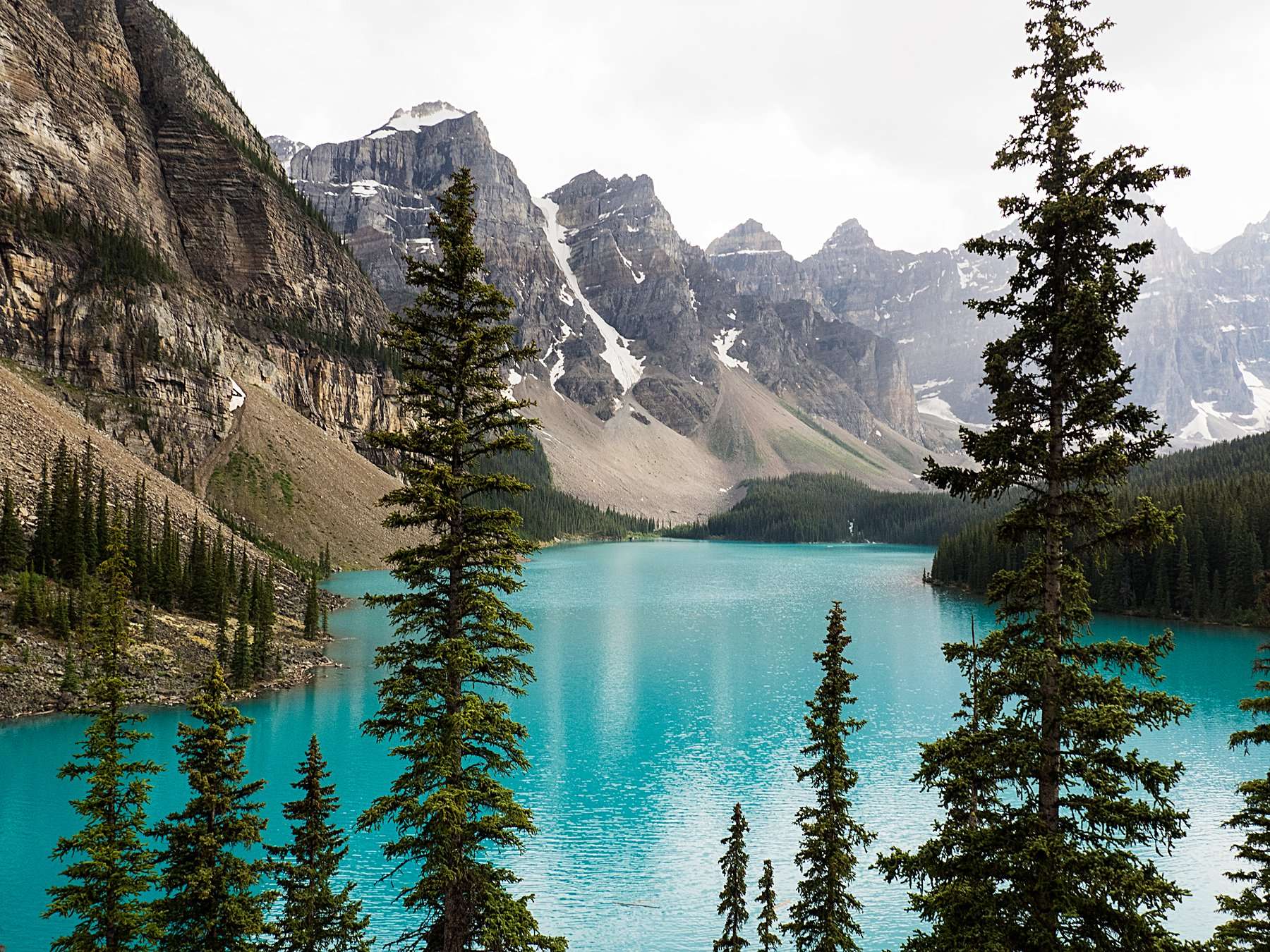 Breathtaking view of turquoise water surrounded by snow-capped peaks and evergreen trees in the mountains—an ideal scene to showcase how to take amazing photos while traveling in nature.