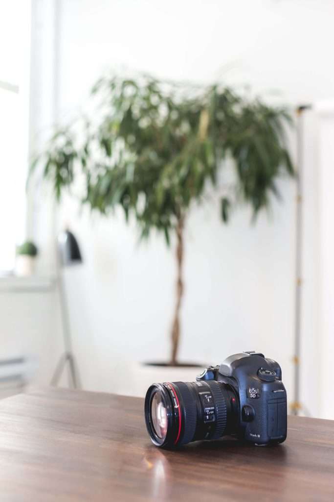 Canon EOS 5D Mark III camera with a prime lens resting on a wooden table in a softly lit studio, representing the importance of using quality gear when striving for tack sharp images.