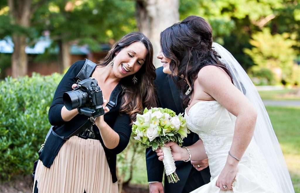 wedding photographer smiling and showing a photo to a bride on the back of her camera.