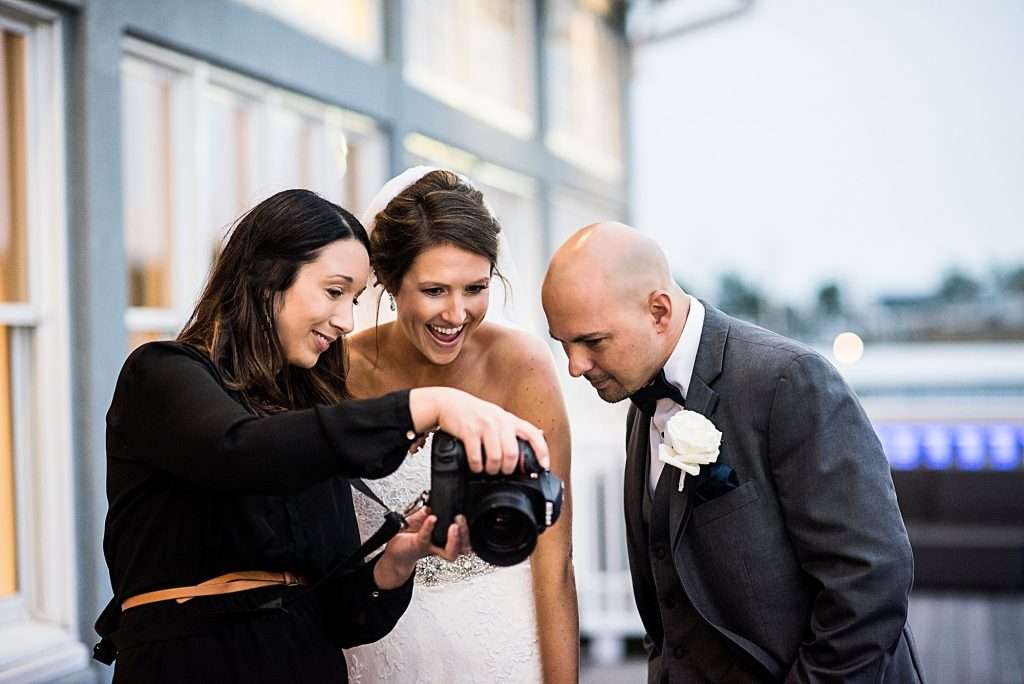 wedding photographer and showing a photo to a bride and groom from the back of her camera.