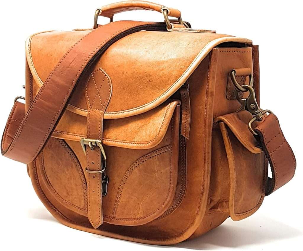 Vintage inspired brown leather camera satchel with buckle closures, multiple front pockets, and a wide adjustable shoulder strap. The rugged leather texture and roomy compartments make it a practical and stylish option for carrying photography gear.