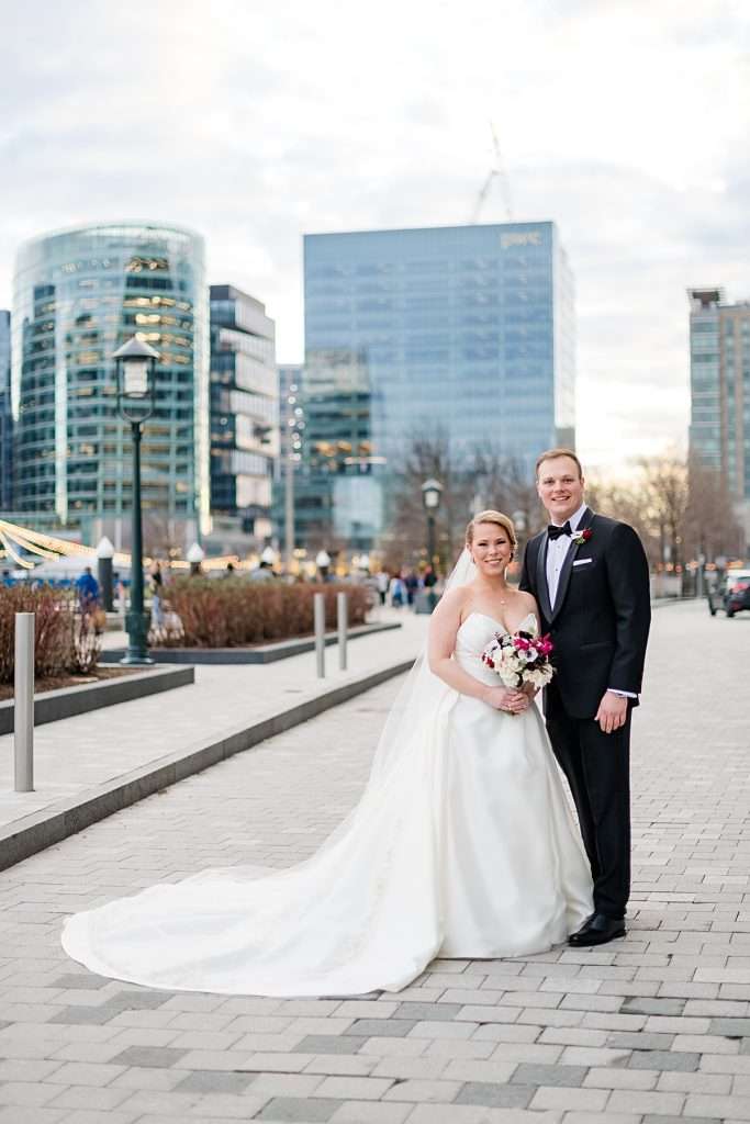 Bride and groom standing on a city sidewalk with buildings softly blurred in the background, showing shallow depth of field with a low aperture setting in camera settings for beginners.