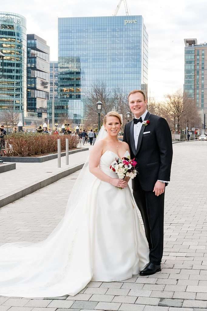 Bride and groom standing on a city sidewalk with buildings, people, and details sharply in focus, showing deep depth of field with a high aperture setting for camera settings for beginners.